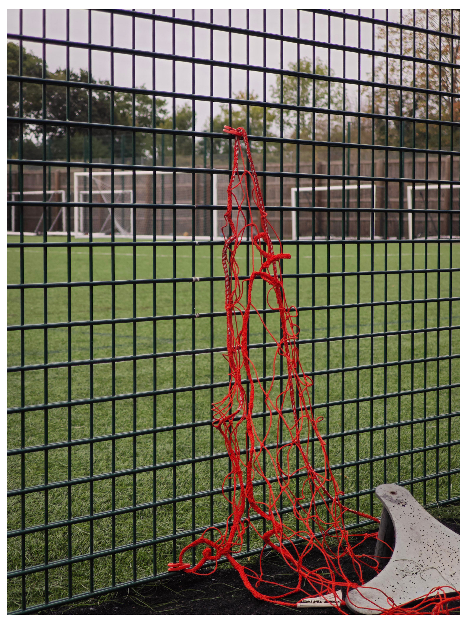 A net hanging from a mesh fence in front of a football pitch